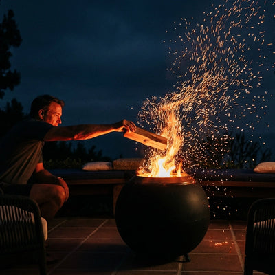Person lighting a fire in a fire pit with sparks flying at night.